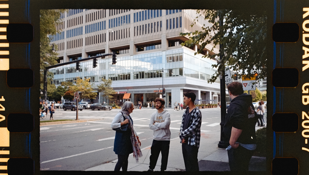 A group of four people engaged in conversation on a bustling city street with modern buildings and greenery in the background.