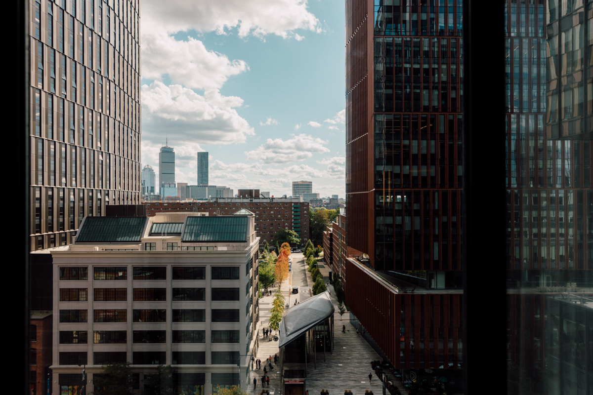A panoramic view of a city skyline featuring modern buildings and a bustling street below, with scattered clouds in the sky.