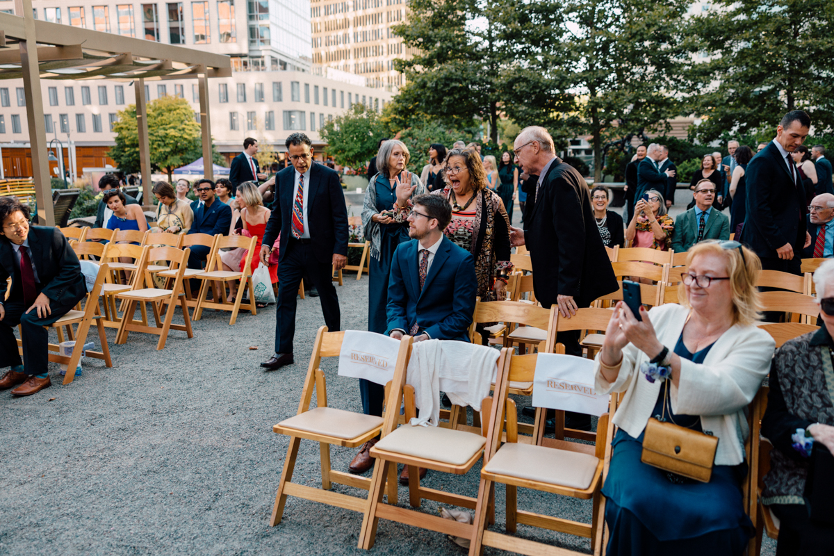 Guests mingling and taking photos at a formal outdoor event with reserved seating.