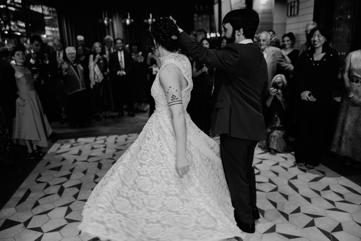 A couple dancing at their wedding reception, surrounded by an enthusiastic audience in a stylish venue.