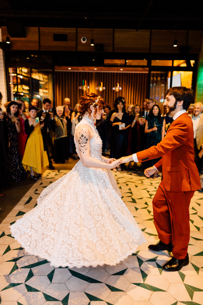 A couple dancing together at their wedding reception, surrounded by guests in a beautifully decorated venue.
