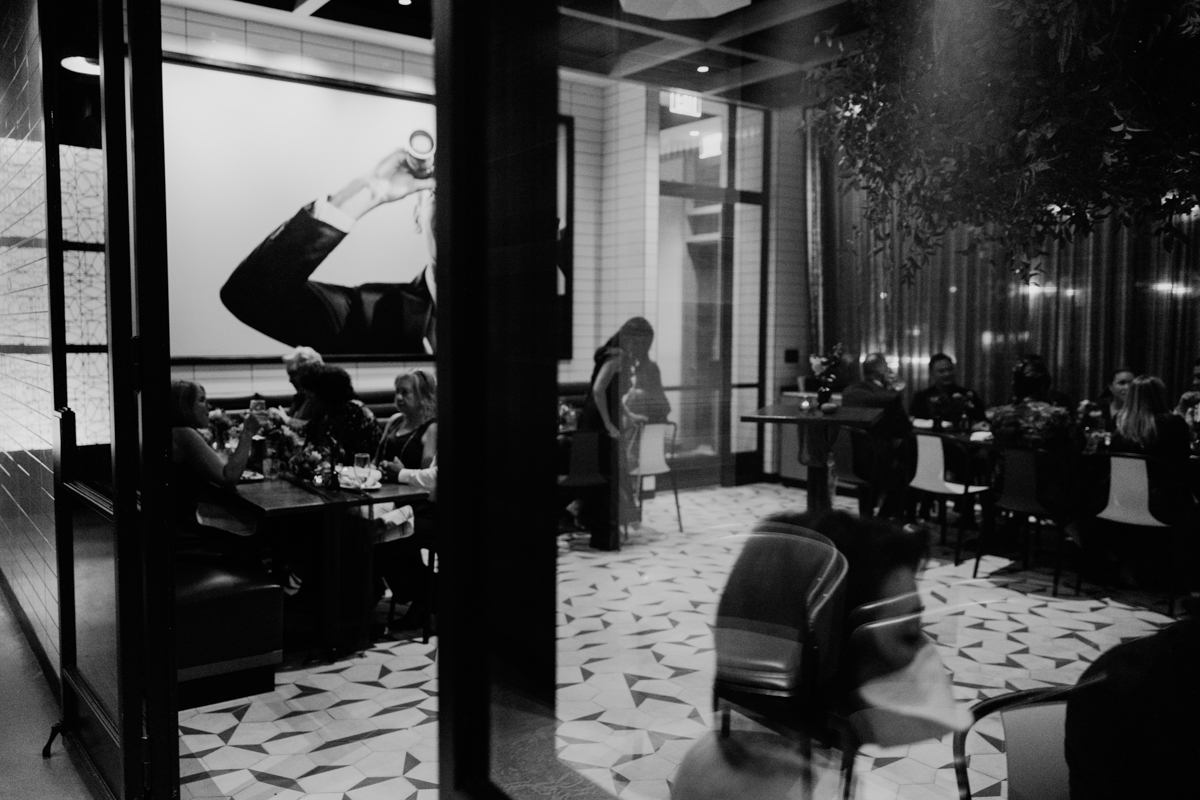 A cozy restaurant scene featuring diners at a table, an abstract photo on the wall, and reflections in glass showcasing a sophisticated ambiance.