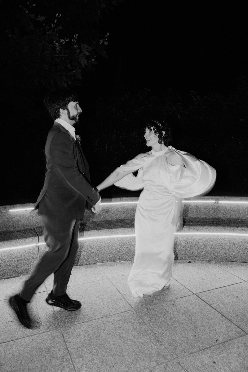 A couple dances joyfully at night, surrounded by softly illuminated seating, capturing a romantic moment.