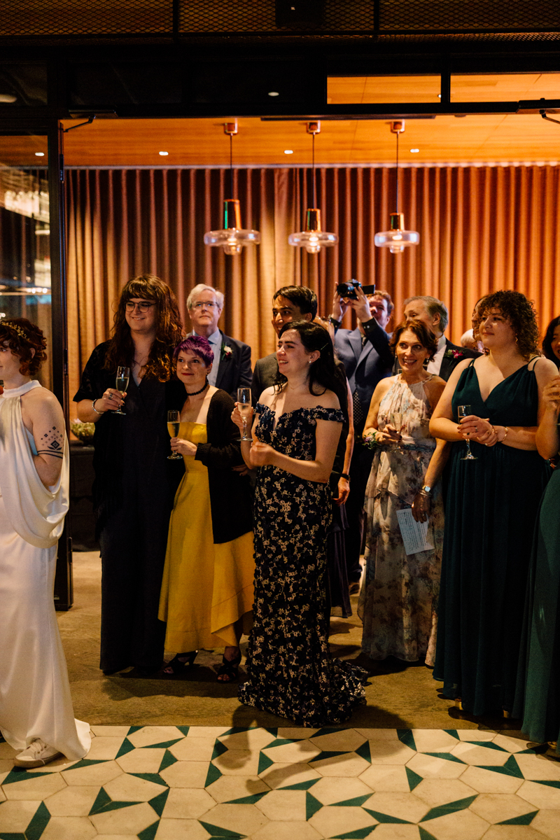 A diverse group of people dressed in formal attire, enjoying a celebration, with drinks in hand and a cozy, stylish venue in the background.