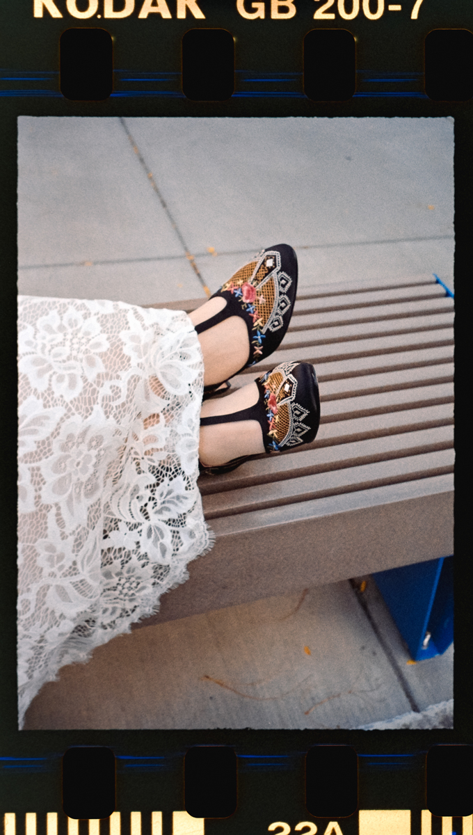 Close-up of embroidered shoes paired with a delicate lace dress, resting on a wooden bench.