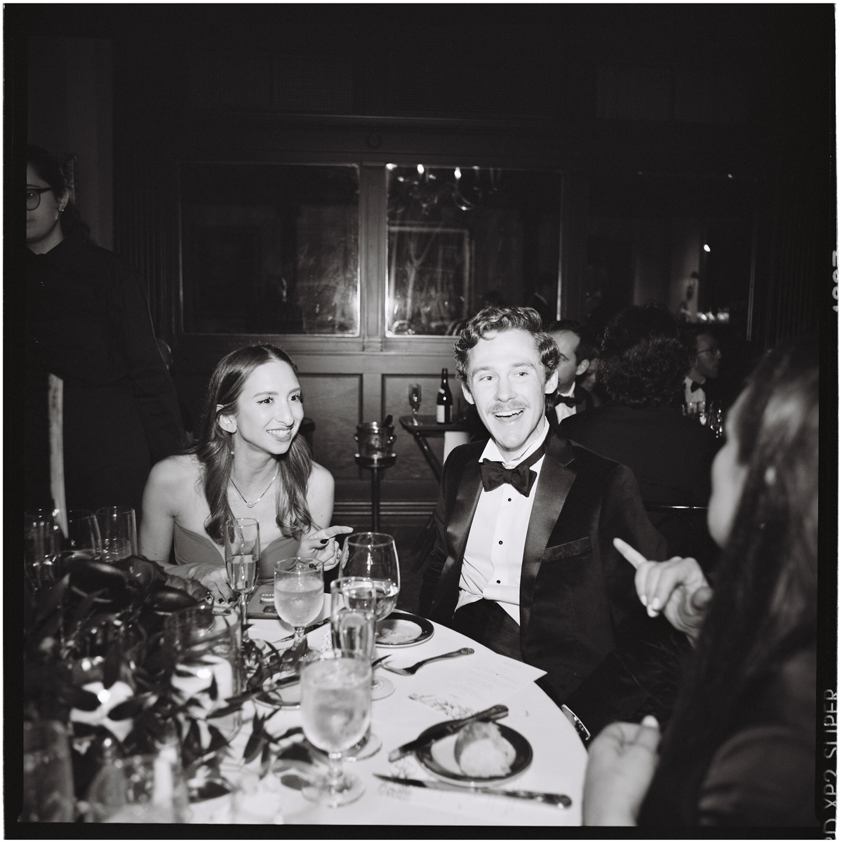 A joyful couple seated at an elegant dinner table, laughing and engaging in conversation, with a festive atmosphere and elegantly set dinnerware.