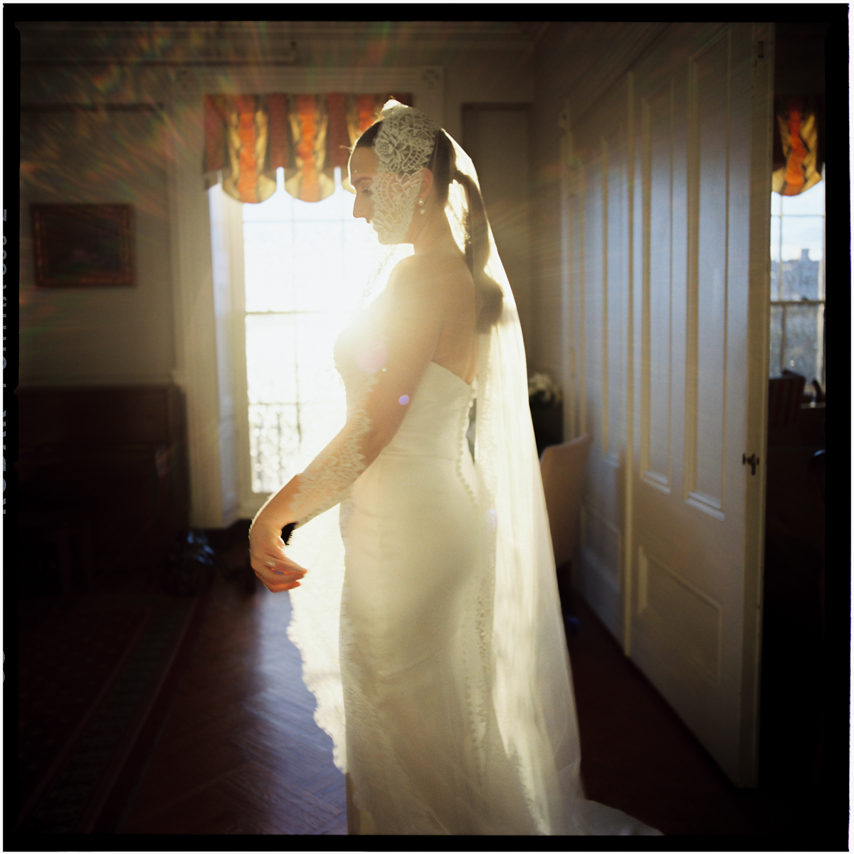 A bride in a flowing white gown and veil stands gracefully in a sunlit room, capturing a moment of serene beauty.