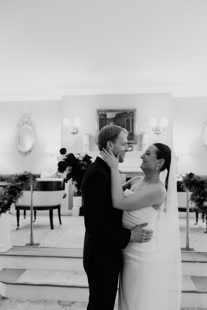 A joyful bride and groom embrace, sharing a loving smile in an elegant indoor setting.