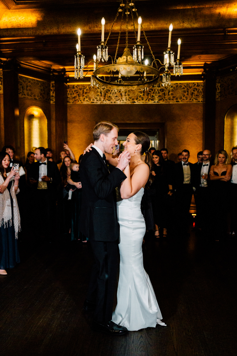 A couple shares an intimate moment while dancing at a beautifully decorated venue, surrounded by guests enjoying the celebration.