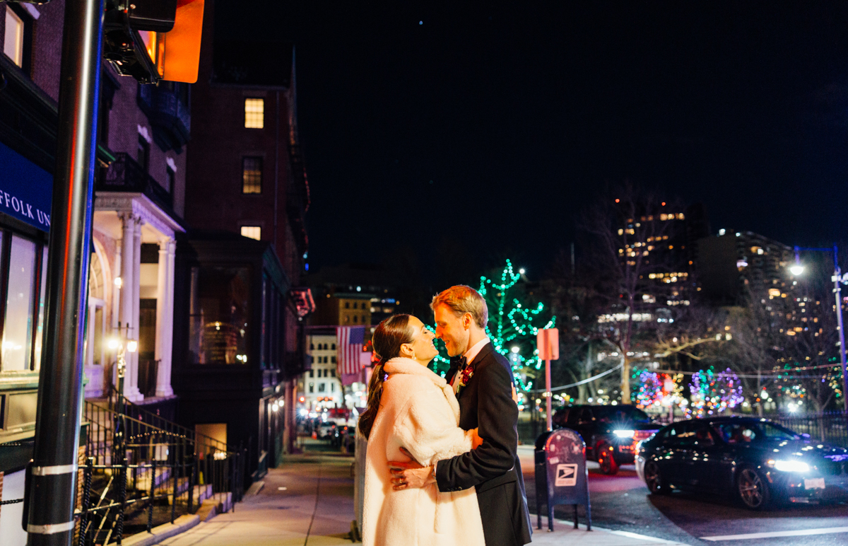 A couple kisses warmly on a city street illuminated by colorful lights during the night.
