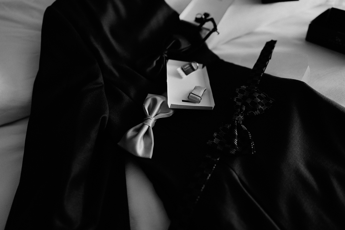 A close-up of a black suit with a silver bow tie and cufflinks placed on a white surface.