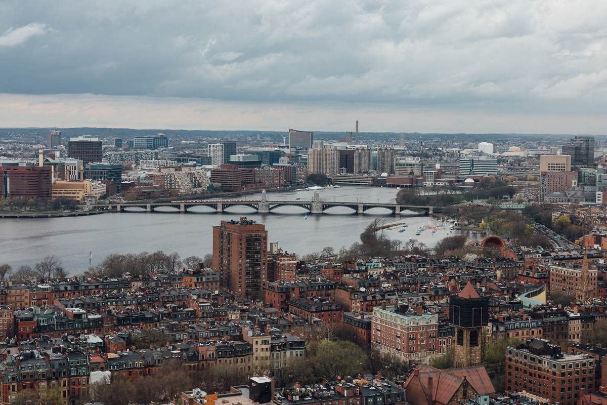 Aerial view of Boston's skyline with the Charles River, featuring historic buildings and modern architecture under a cloudy sky.