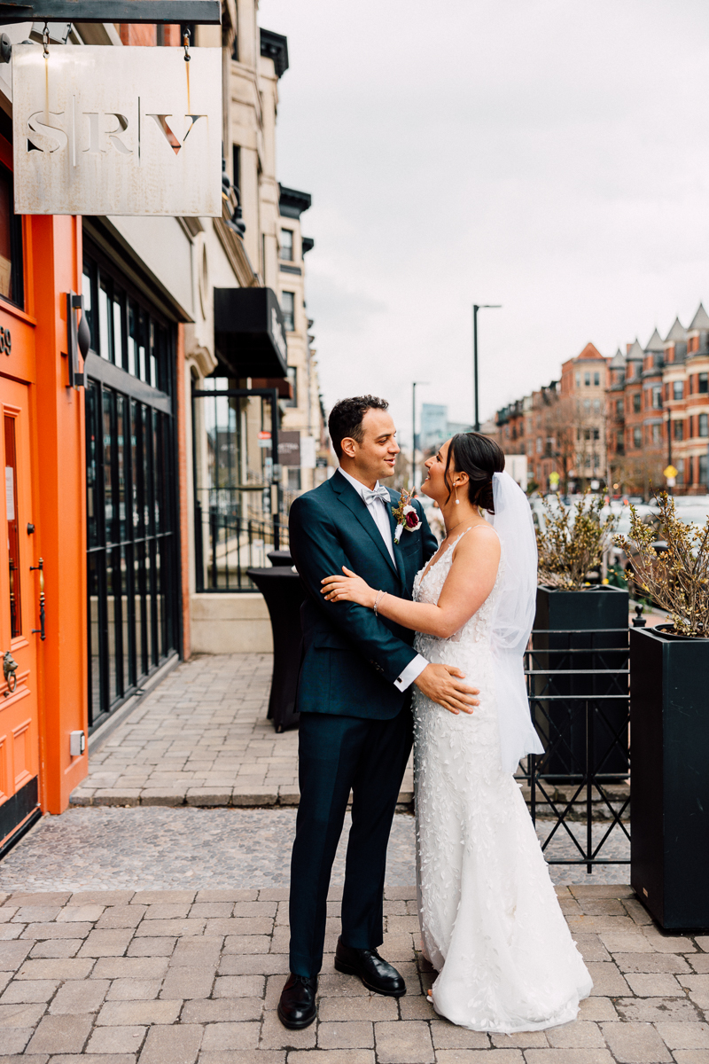 A joyful couple embraces outside a boutique venue, showcasing love and elegance on their special day.