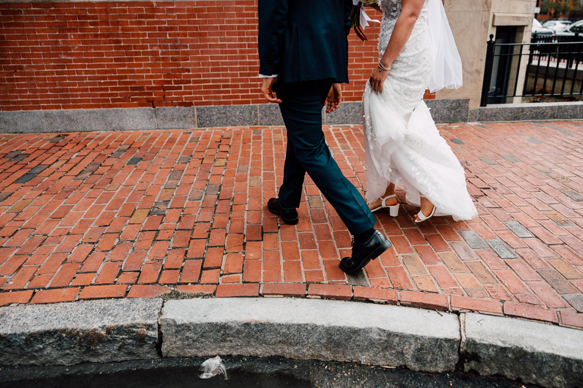 Bride and groom walking together on a brick-paved street, showcasing their wedding attire.
