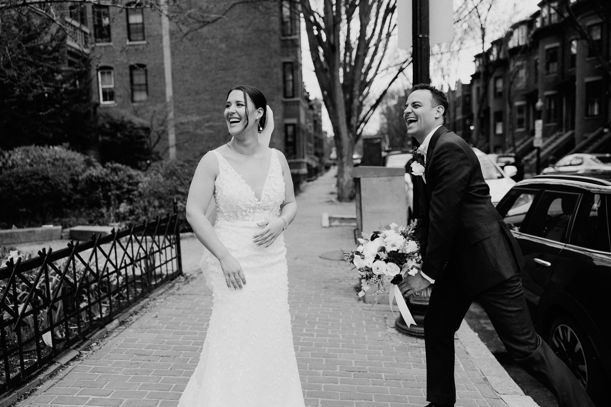 A bride and groom laughing together on a city street, capturing a candid moment of happiness before their wedding ceremony.