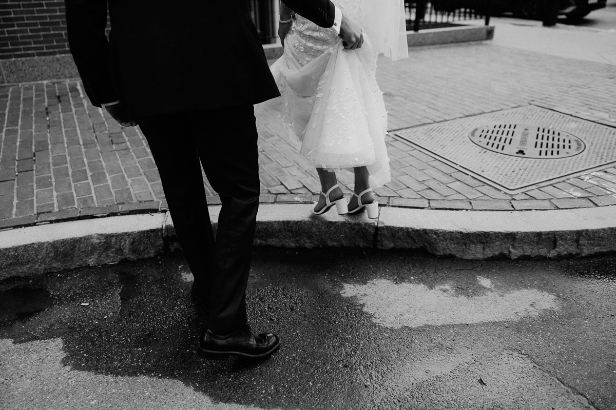 A close-up of a groom assisting a bride in her wedding dress as she steps onto the curb, showcasing love and support.