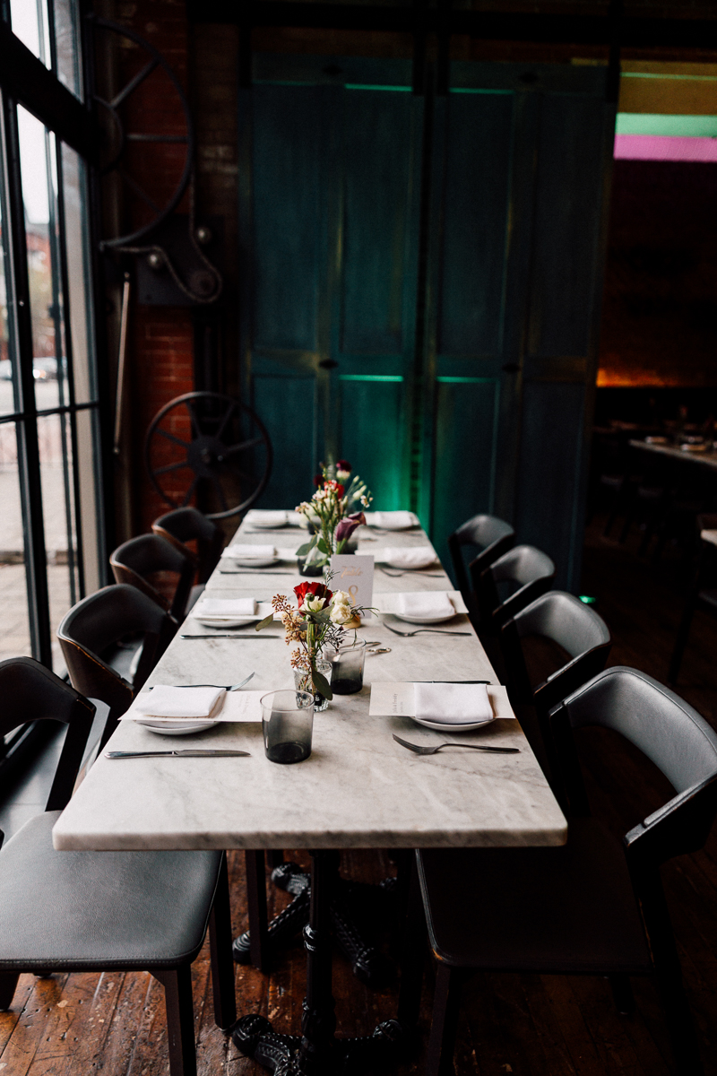 A spacious dining table adorned with floral centerpieces and neatly set with plates and utensils, surrounded by stylish black chairs in a warm, atmospheric interior.