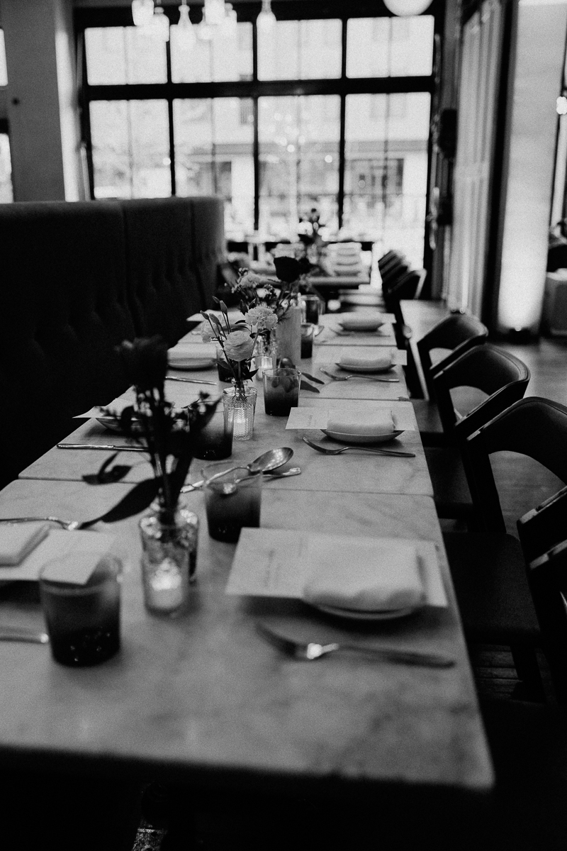 A beautifully arranged table with flowers, plates, and cutlery, set against large windows in a stylish restaurant.