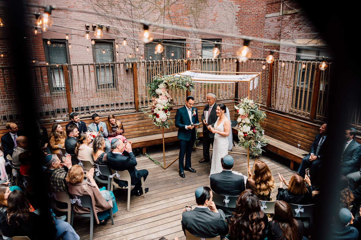 A couple exchanges vows during an intimate outdoor wedding ceremony, surrounded by family and friends in a beautifully decorated space.