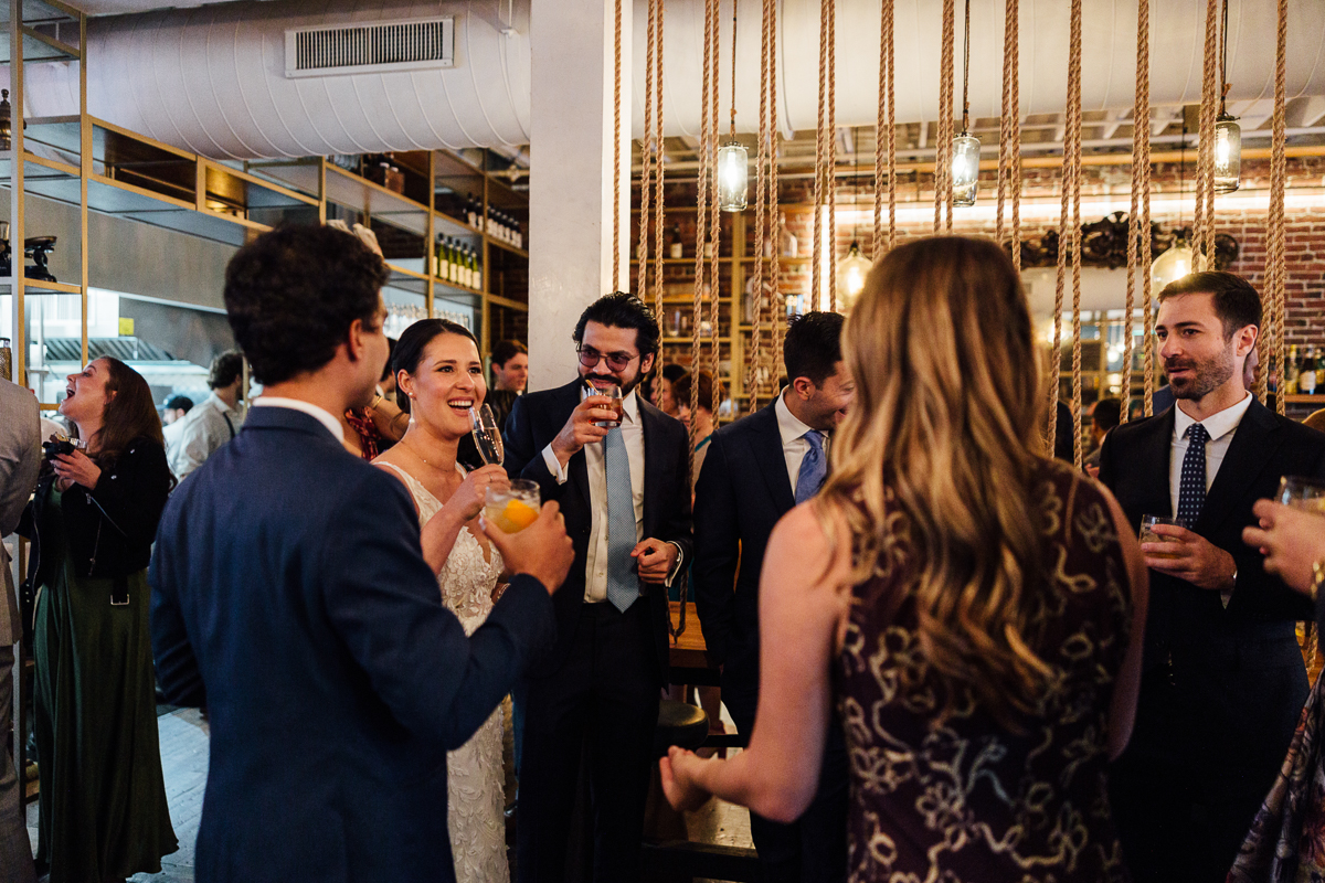 A joyful group of well-dressed individuals raising their glasses in celebration at a stylish venue, with a bride in a beautiful gown smiling in the center.