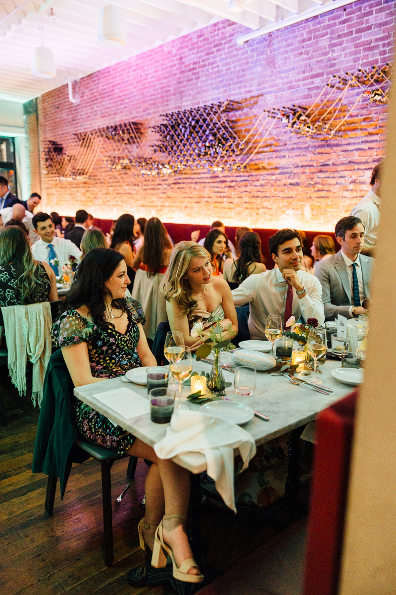 Guests enjoying dinner at a stylish restaurant with a warm ambiance, featuring a brick wall and tasteful table settings.