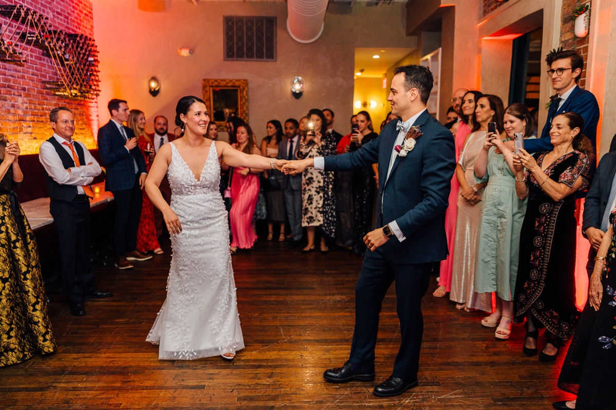 A joyful couple performing their first dance at a wedding reception, surrounded by family and friends enjoying the moment.