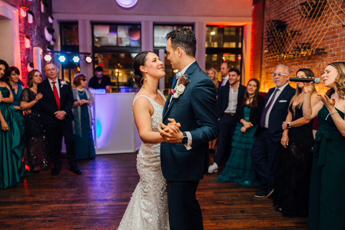 A couple shares a romantic first dance at their wedding, surrounded by guests enjoying the moment in a beautifully decorated venue.