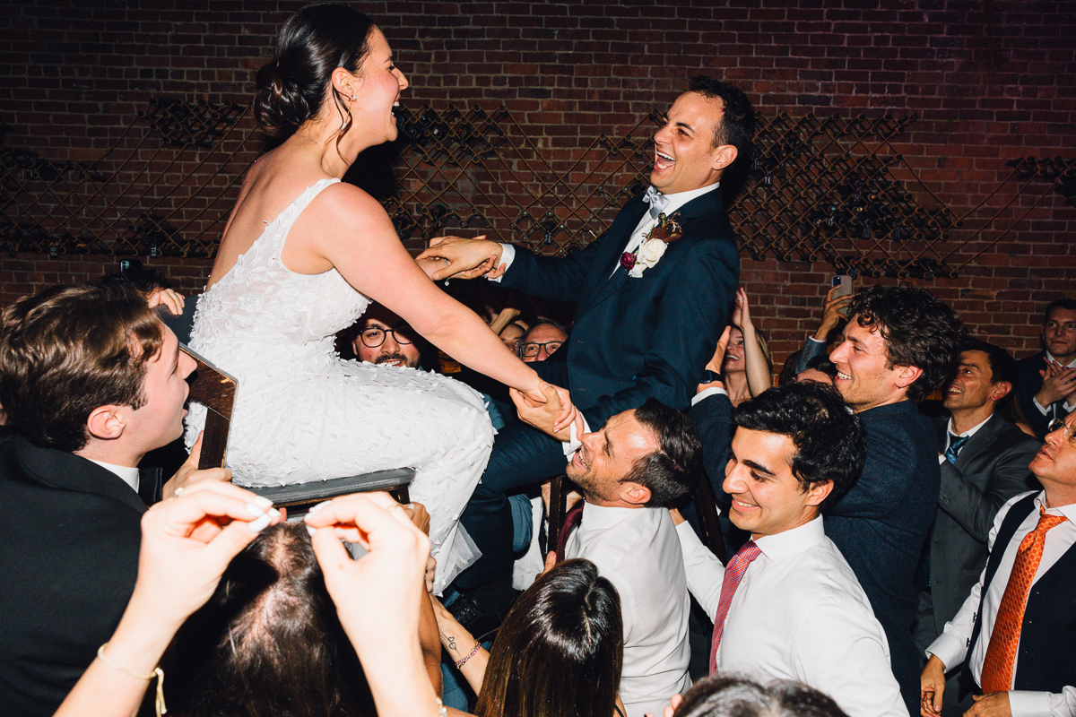 Bride and groom joyfully lifted in celebration by guests at a wedding reception.