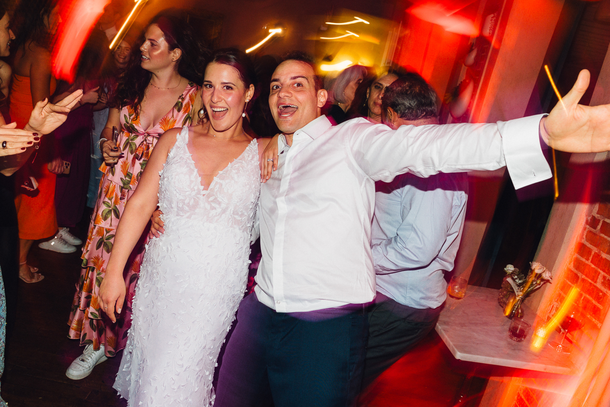 A bride and a guest joyfully celebrating together on the dance floor, surrounded by a lively party atmosphere.