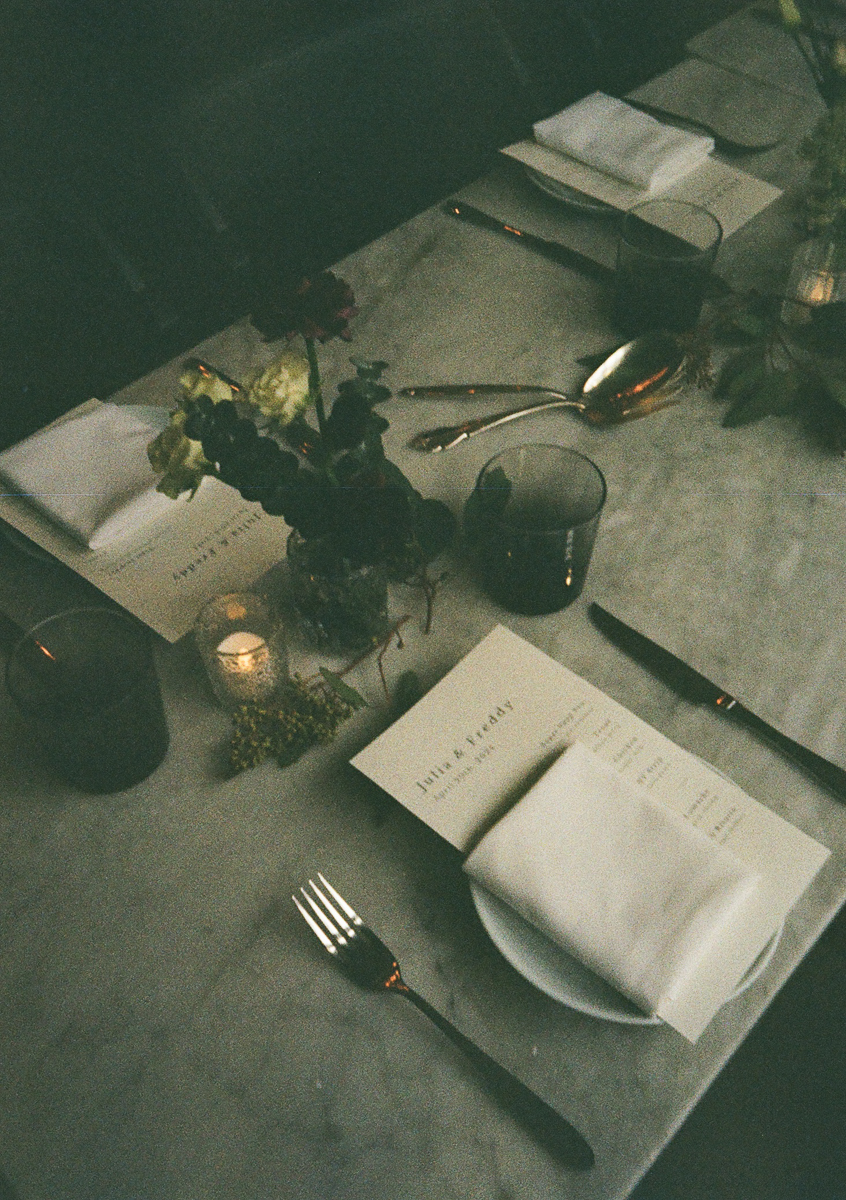 A beautifully set table featuring a marble surface, decorative floral arrangements, menus, and elegant tableware, all set in a dimly lit ambiance.