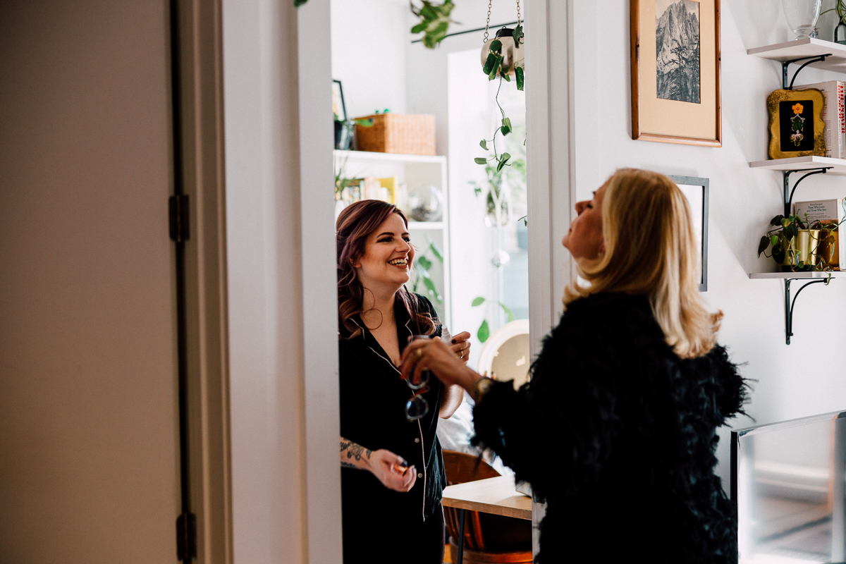 Two women sharing a moment of joy in a warmly decorated room filled with plants and personal touches.