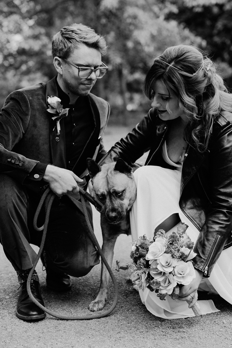 A couple kneels together, gently interacting with their dog while surrounded by nature, capturing a heartfelt moment on their special day.