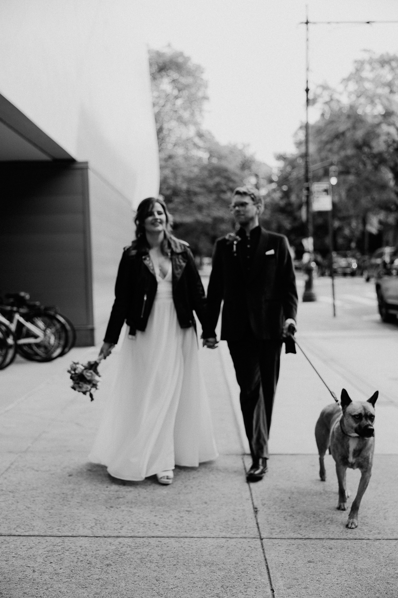 A couple walking hand-in-hand on a city sidewalk, accompanied by their dog, exuding joy in a modern urban setting.