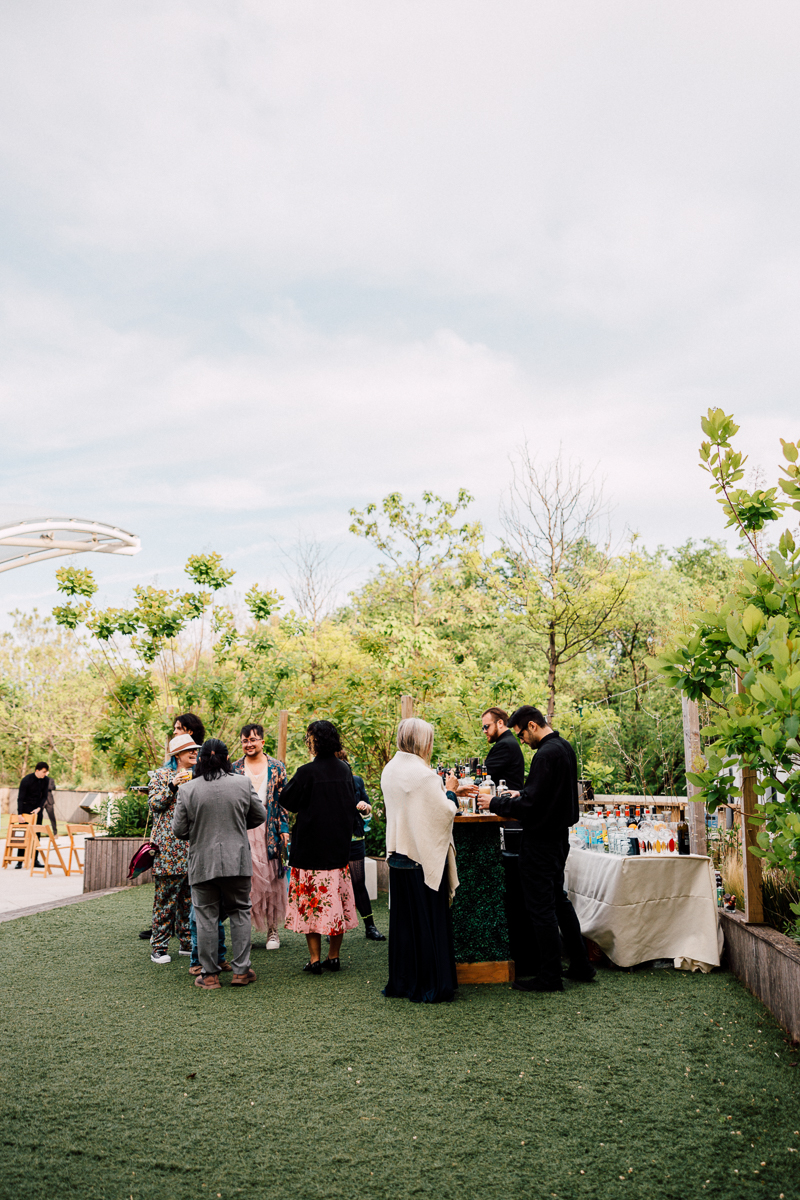 Guests socializing around a bar in a lush green setting on a cloudy day.