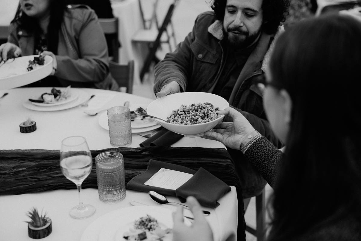 Guests at a dining table passing a bowl of grain dish during a meal.