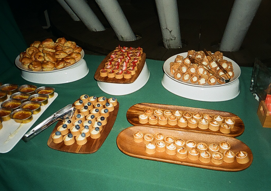A variety of elegantly presented desserts including pastries, tarts, and creamy treats arranged on wooden platters and a green tablecloth.