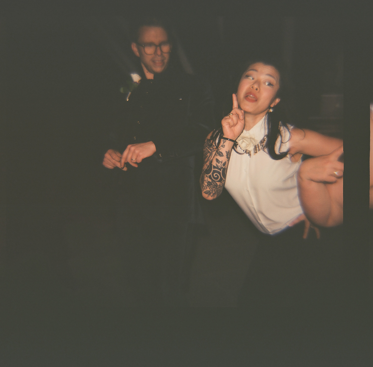 A woman with a tattoo poses playfully while a man smiles in the background, capturing a lively atmosphere.