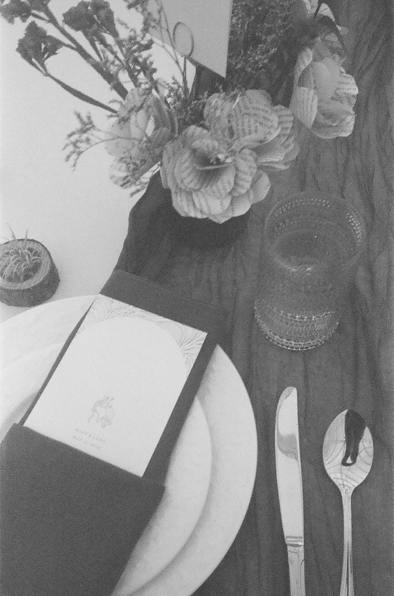 A beautifully arranged dining table featuring floral decorations, a menu, plates, and cutlery, captured in black and white.
