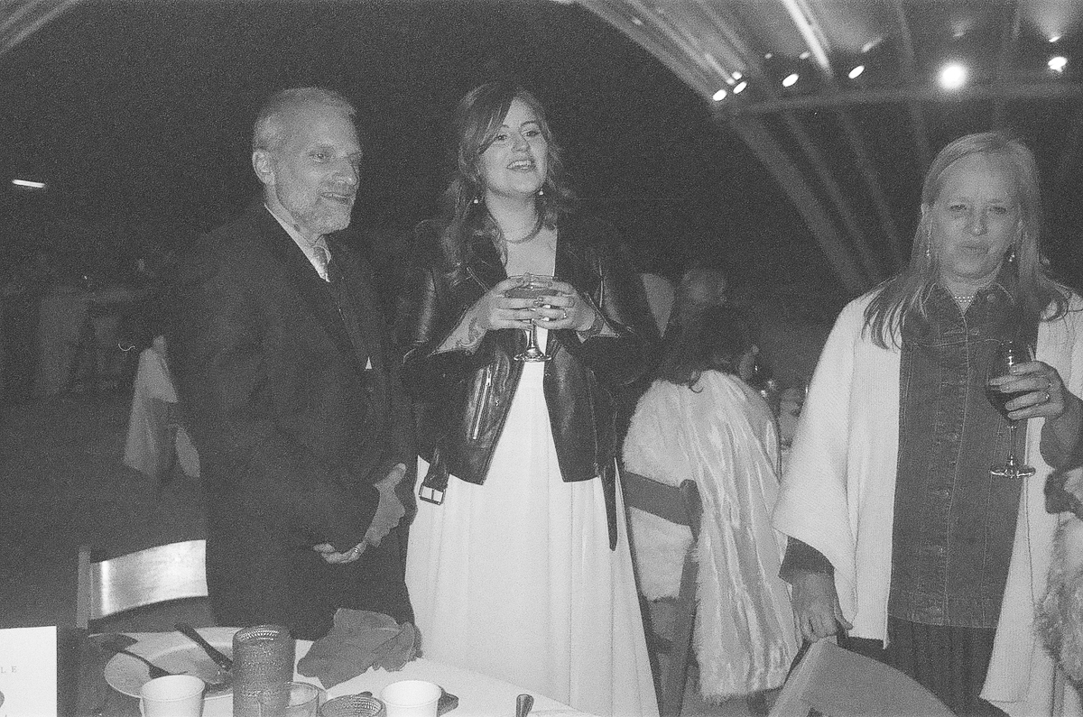 Three people enjoying a social event, one holding a drink, with a warm ambiance in the background.