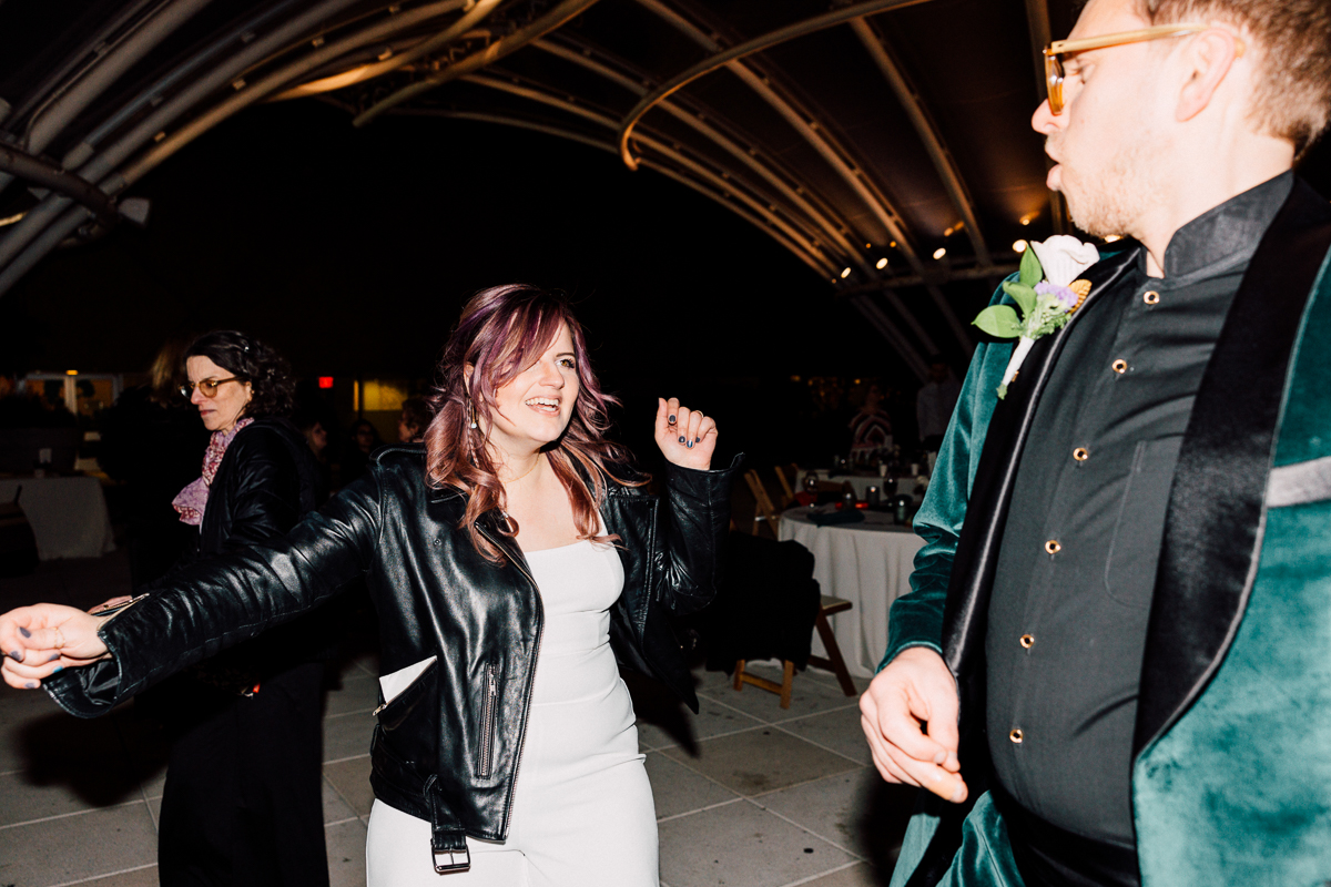A lively scene of a woman in a leather jacket enjoying herself while dancing at a nighttime event, with another guest in a green jacket nearby.