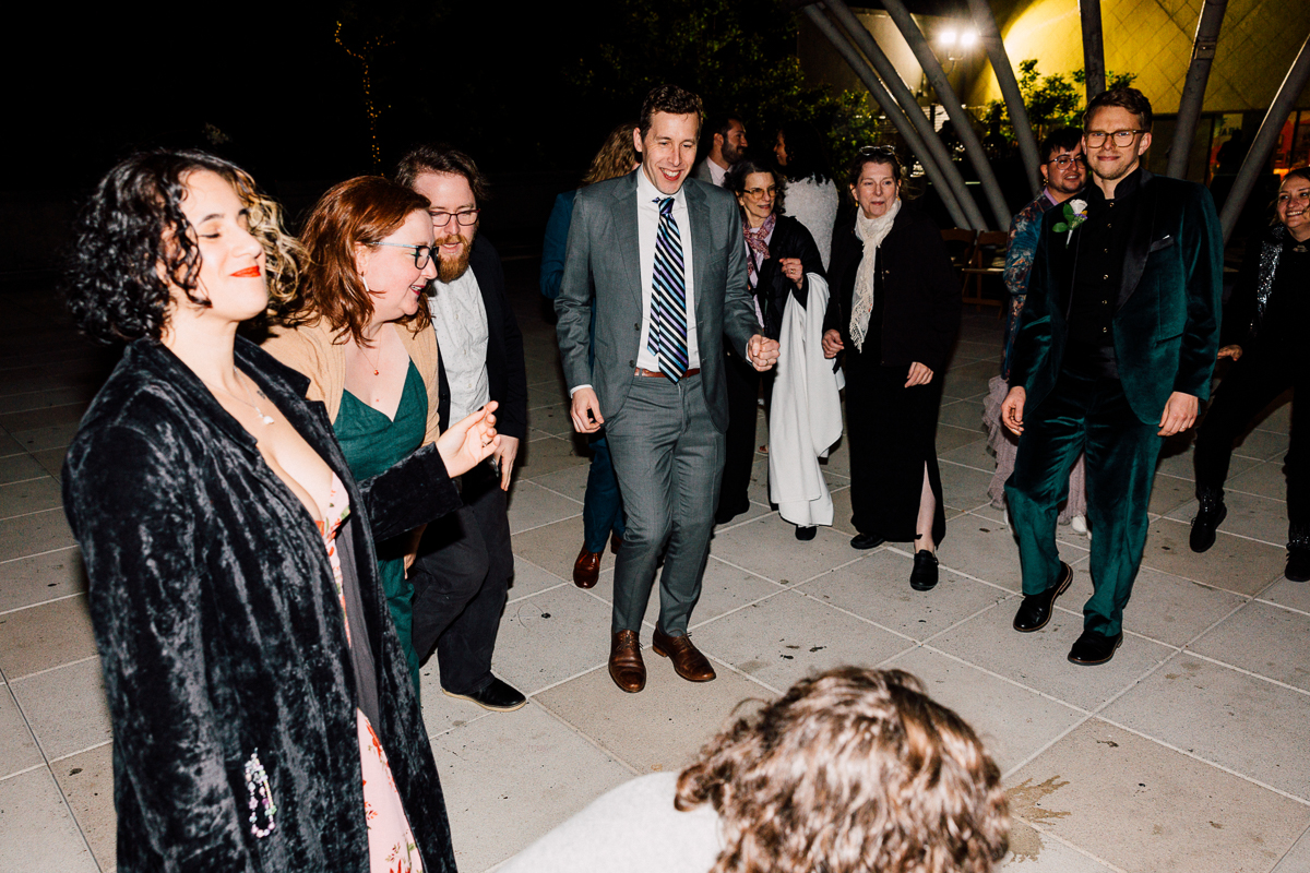 A lively group of people dancing together outdoors at night, dressed in formal attire and enjoying the festive atmosphere.