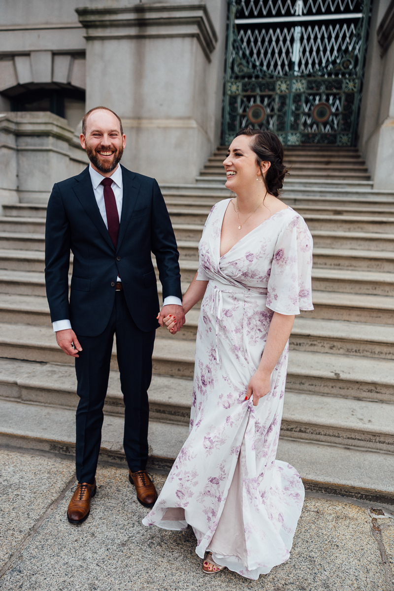 A smiling couple stands hand-in-hand on outdoor steps, dressed elegantly for a special occasion.