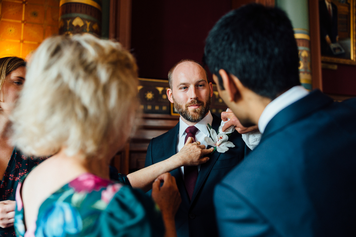 Groom Getting Ready::A group of people helping a groom prepare for an event, adjusting his boutonnière in an elegant setting.