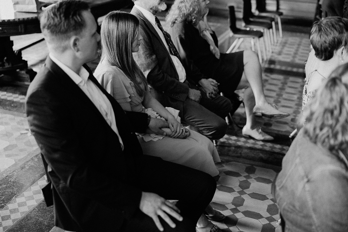 A close-up of seated guests during a special occasion, showcasing the connection between individuals as they hold hands, surrounded by an elegant setting.