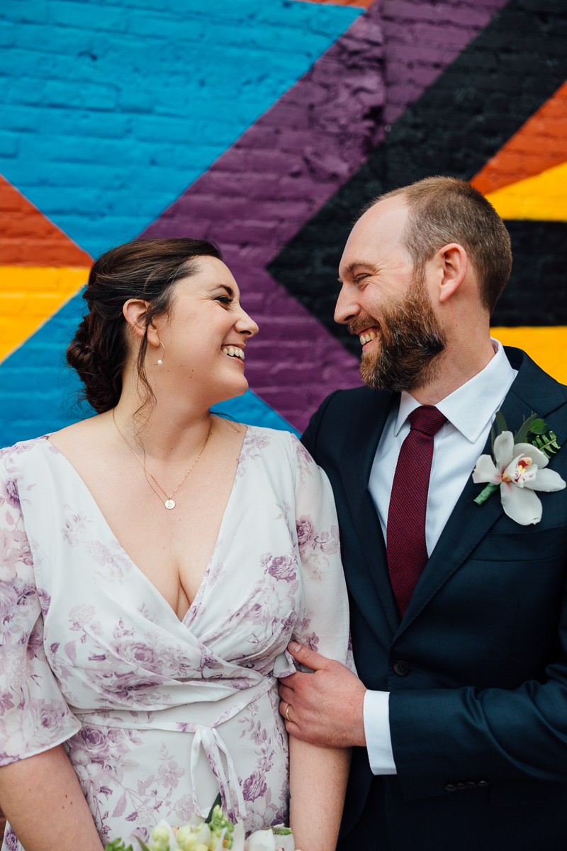 A smiling couple shares a loving moment in front of a vibrant mural, showcasing their joy and connection on a special occasion.