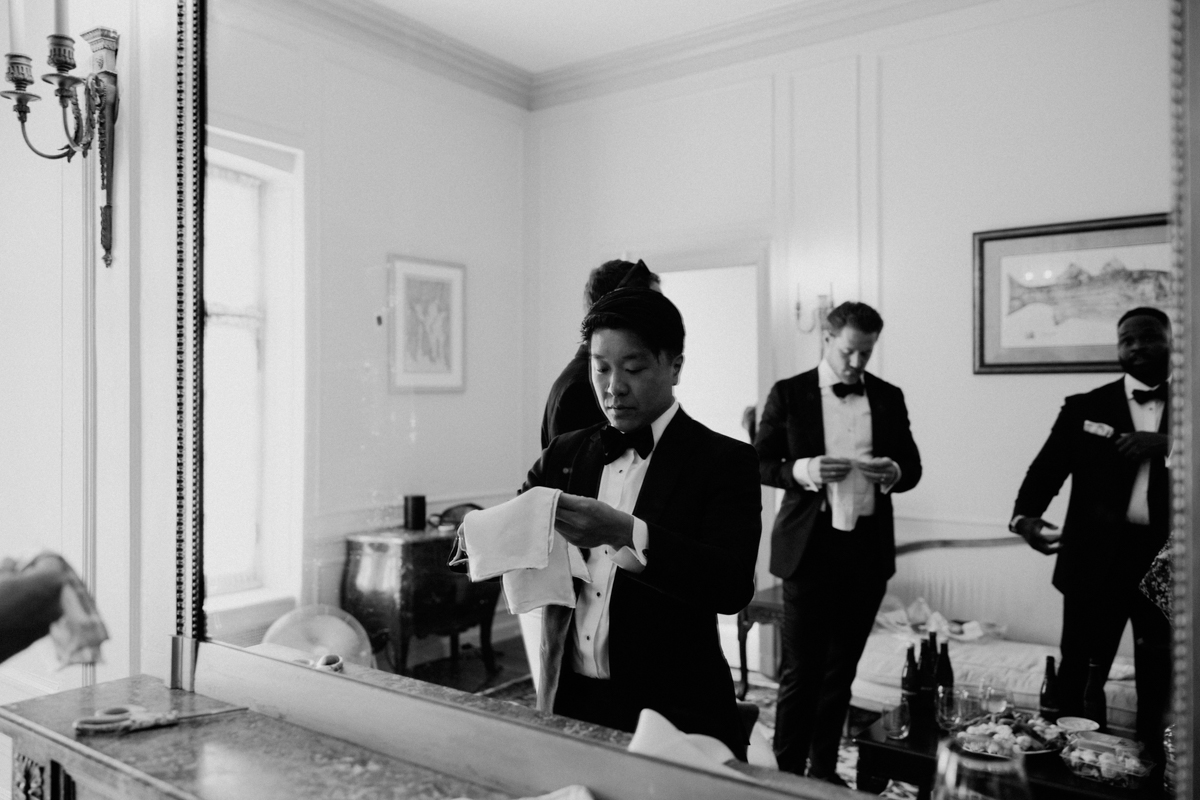 A group of well-dressed individuals in a mirror reflection, one adjusting a napkin while others are preparing off to the side.