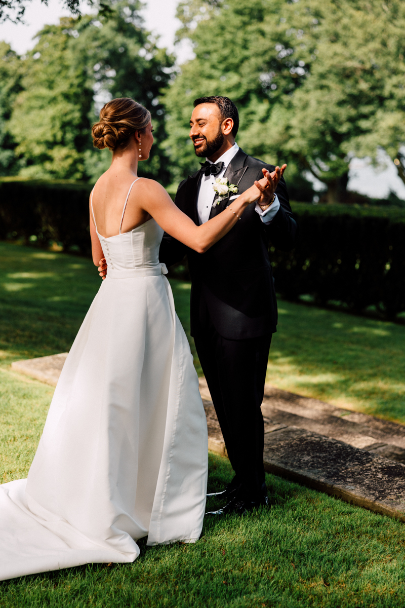 A bride and groom share a joyful moment dancing together in a lush outdoor setting, showcasing their love and happiness.