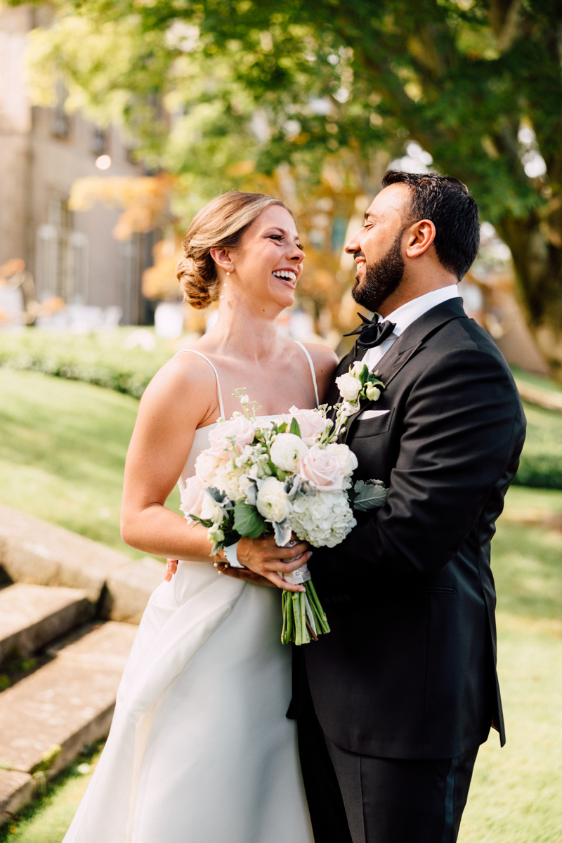 A bride and groom share a loving gaze, surrounded by lush greenery, as the bride holds a beautiful bouquet of flowers.
