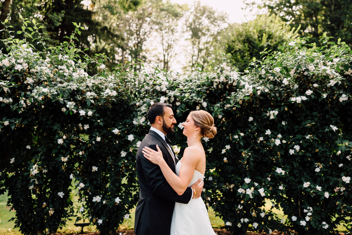 A joyful couple embracing in front of a blossoming hedge, radiating love and happiness on their special day.