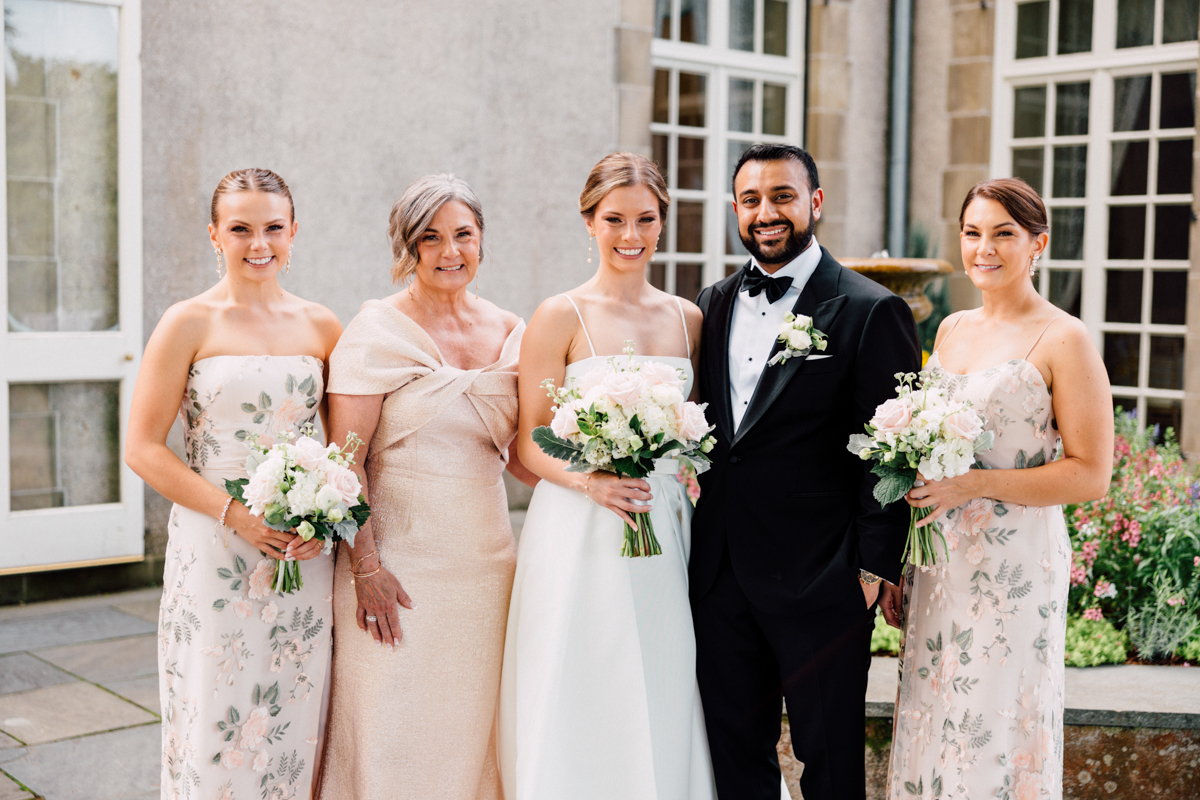 A joyful couple stands with their bridal party outside, surrounded by flowers, showcasing elegance and celebration in a beautiful setting.